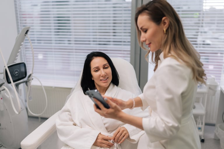 Friendly beautician in white uniform reviewing treatment options with a female client in a private, compassionate consultation setting