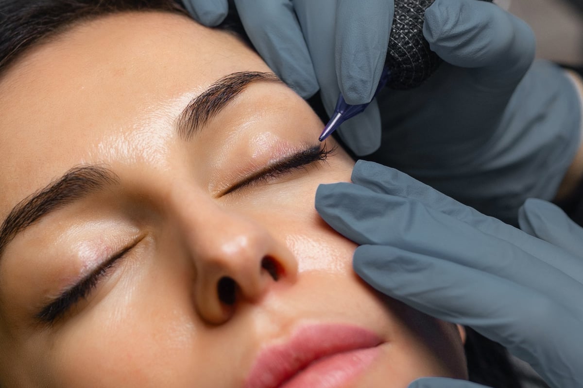 Close up of a cosmetologist performing eyelid permanent makeup, precision eyeliner tattoo procedure with sterile tools, enhancing lash line and eye beauty in a professional studio