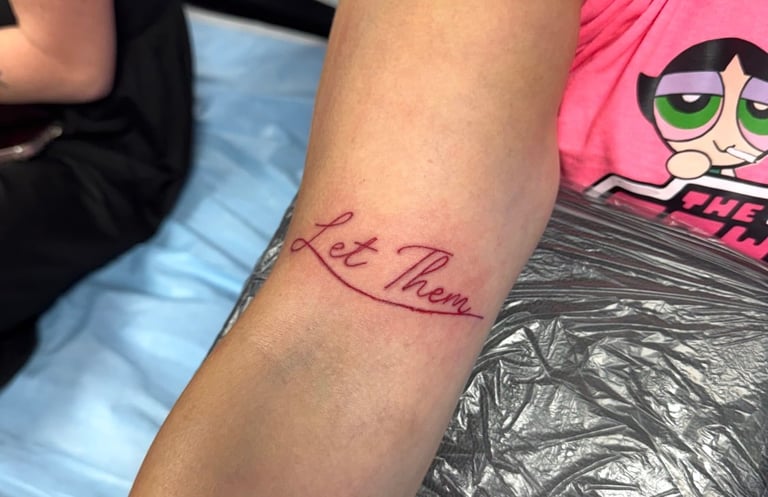 Arm with red cursive tattoo script on forearm near Powerpuff Girls merchandise