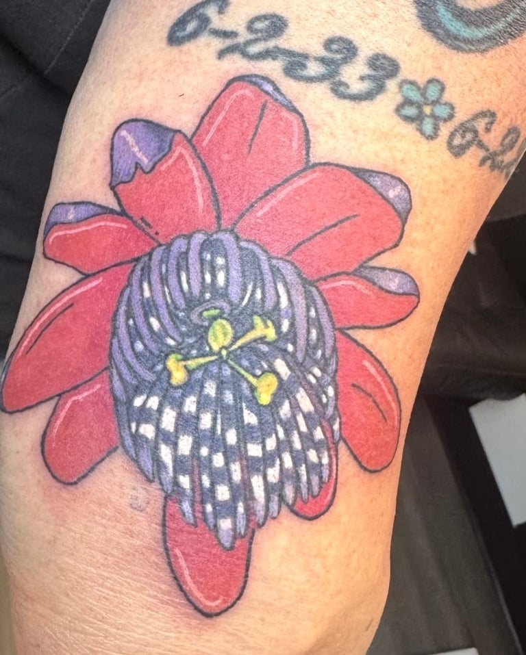 Colorful tattoo of an owl with dark feathered head and yellow eyes nestled in the center of red flower petals on skin