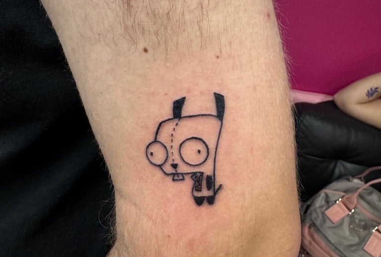 Tattoo of a simple cartoon dog with circular eyes and droopy ears on someone's arm