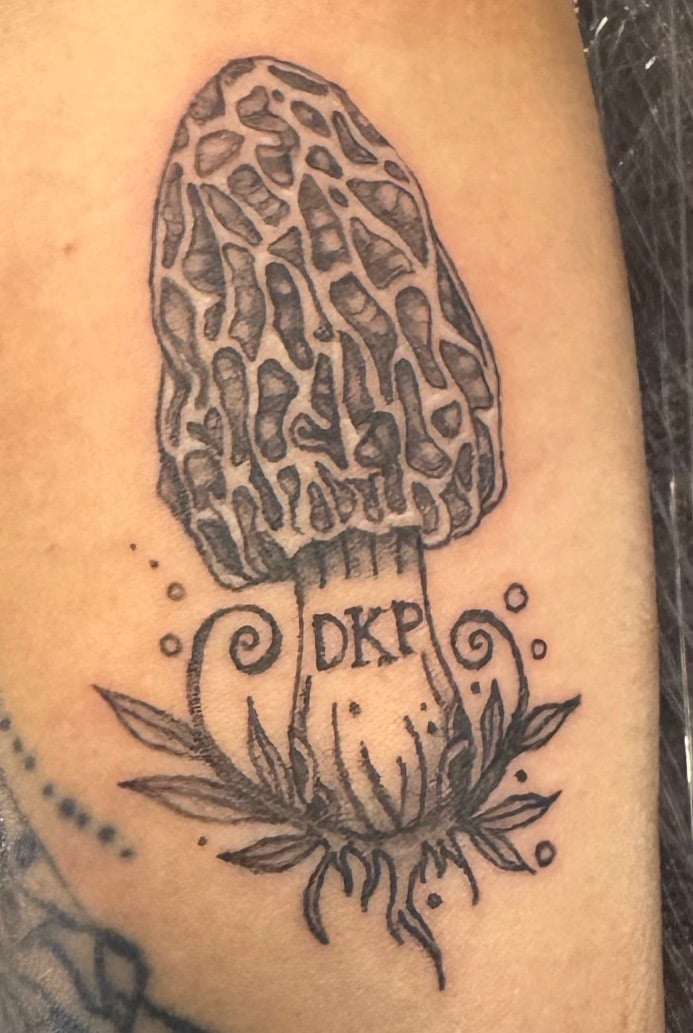 Black ink tattoo of a morel mushroom with DKP initials and decorative leaves on skin