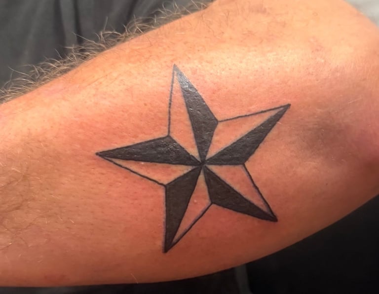 Black five-pointed star tattoo on a person's arm, featuring bold geometric lines with solid shading
