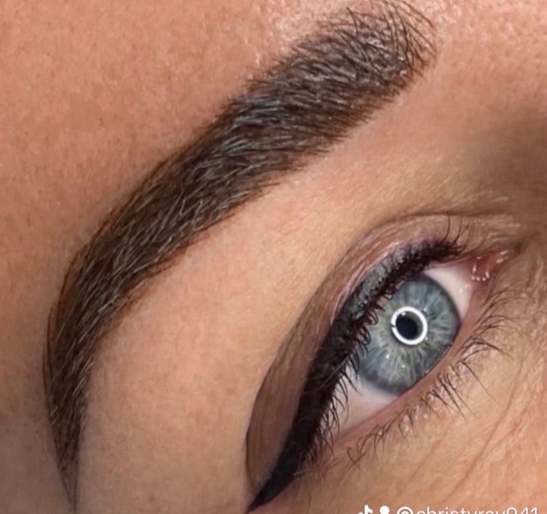 Close-up of a womans eye with blue-green iris, black eyeliner, and dark arched eyebrow
