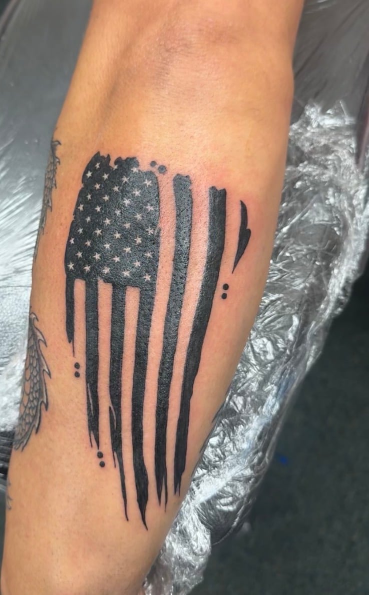 Black American flag tattoo on forearm with stars and vertical stripes design