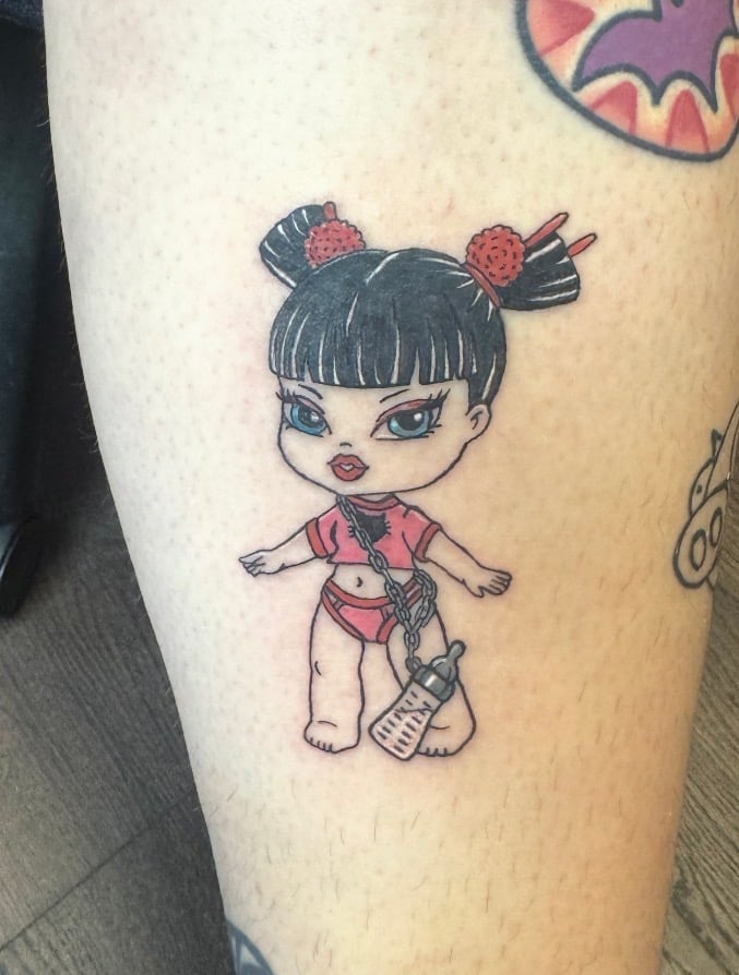 Tattoo of an anime-style girl character with black hair buns, pink outfit, and wrapped leg on light skin