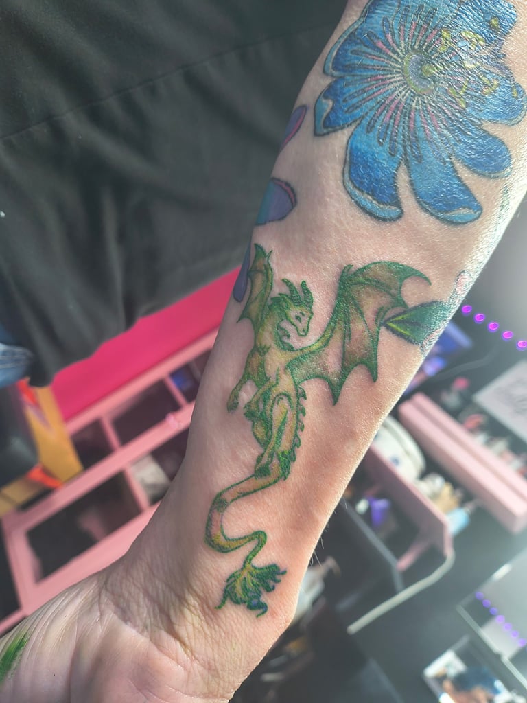 Arm tattoo featuring a blue flower at the top and a green dragon design curving down the forearm
