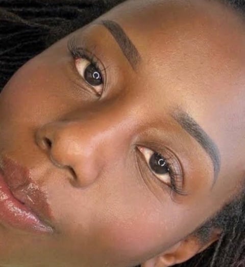 Close-up of a womans face showing professional makeup with defined eyebrows, eye makeup, and nude lip color against a warm skin tone
