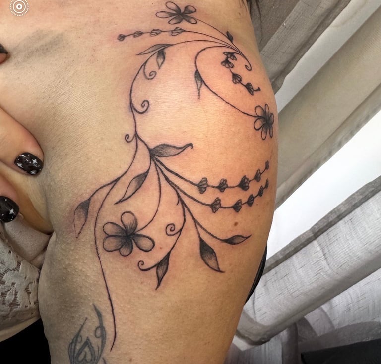 Decorative floral tattoo on upper arm featuring black ink vines, leaves, and flowers in a flowing botanical design