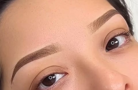 Close-up of a womans face showing defined eyebrows and eyes with makeup, looking upward