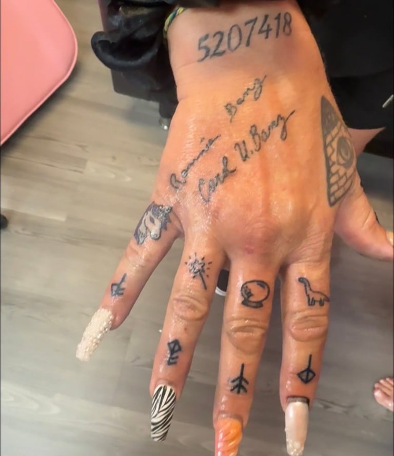 Hand with multiple tattoos including numbers and text on fingers, nails with zebra stripe and orange nail art