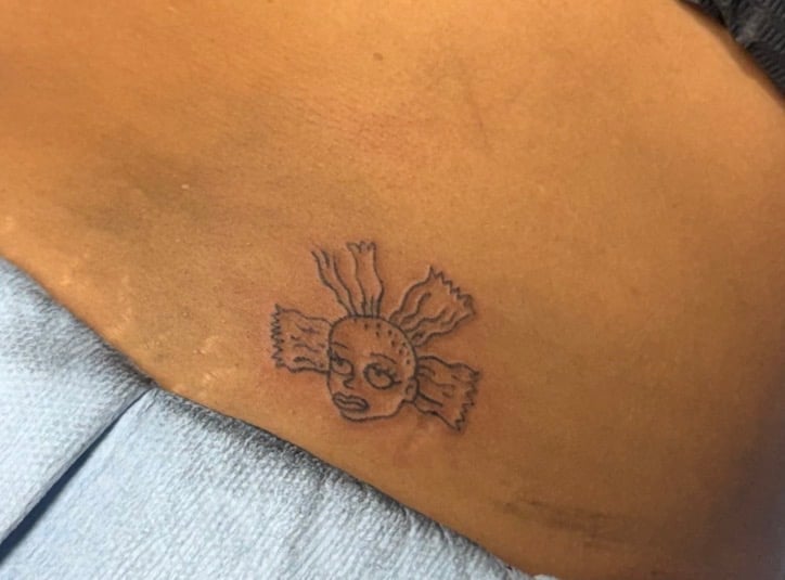 Small black outline tattoo of a skull with wings on tan skin
