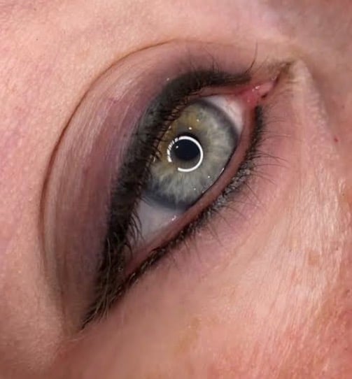 Close-up of a human eye with green iris, dark pupil, black eyeliner, and pink eyeshadow