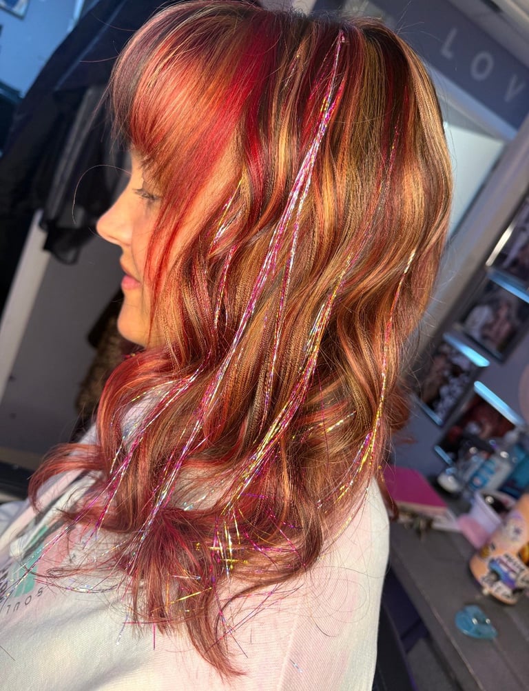 Chunky red lowlights with Fairy Hair at CC Styling Studio in Bradenton, FL — shoulder-length wavy hair featuring red and golden blonde highlights in a salon setting