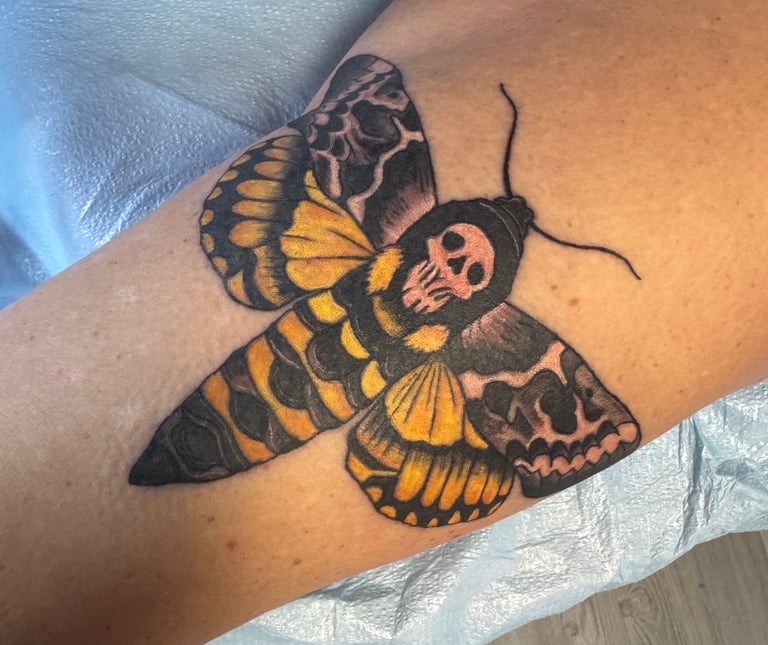 Tattoo of a black and yellow deaths head moth with skull markings on person's arm