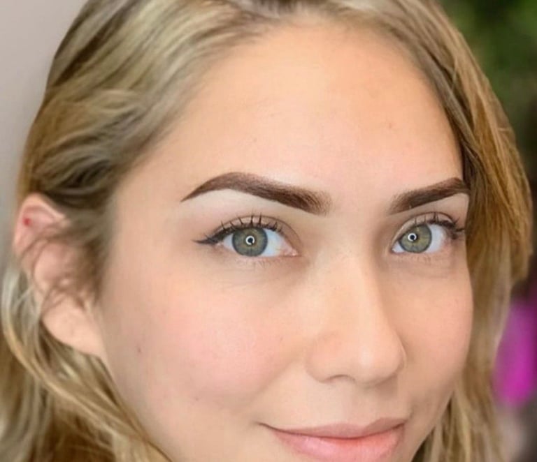 Close-up portrait of a woman with light brown hair, blue-green eyes, and defined eyebrows looking at the camera