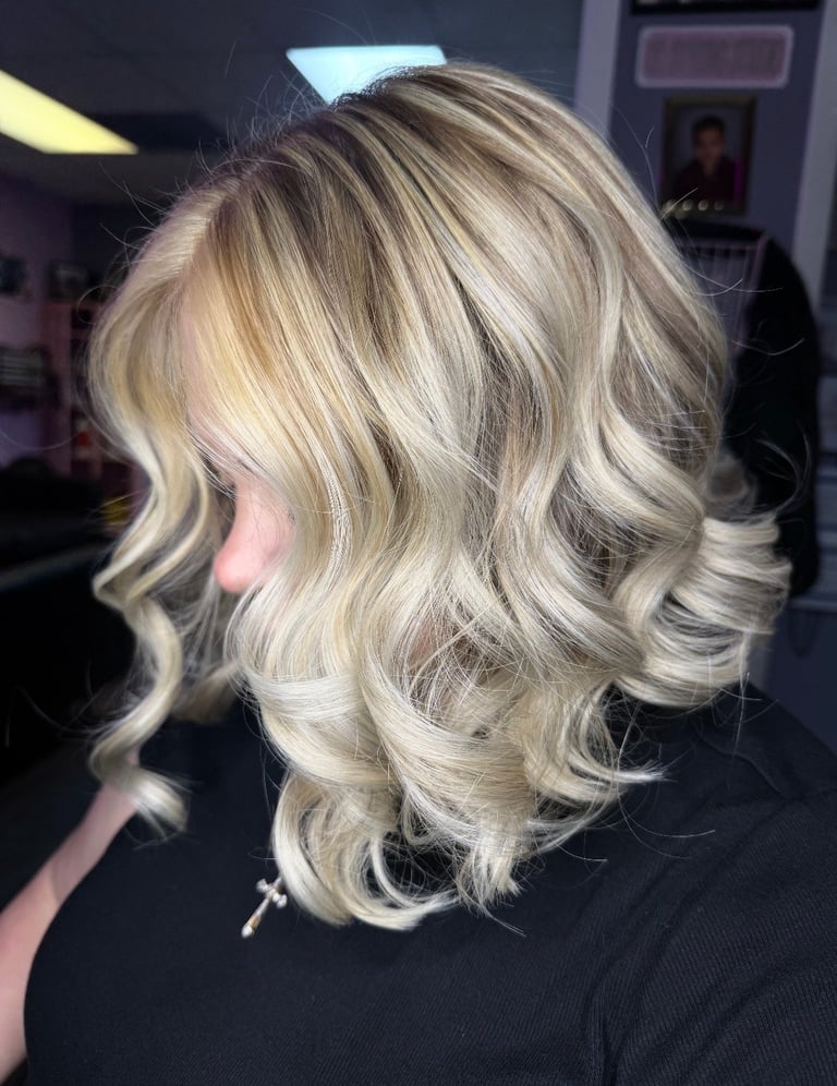Foil lowlights hair color at CC Styling Studio in Bradenton, FL — shoulder-length blonde hair styled in loose waves viewed from behind