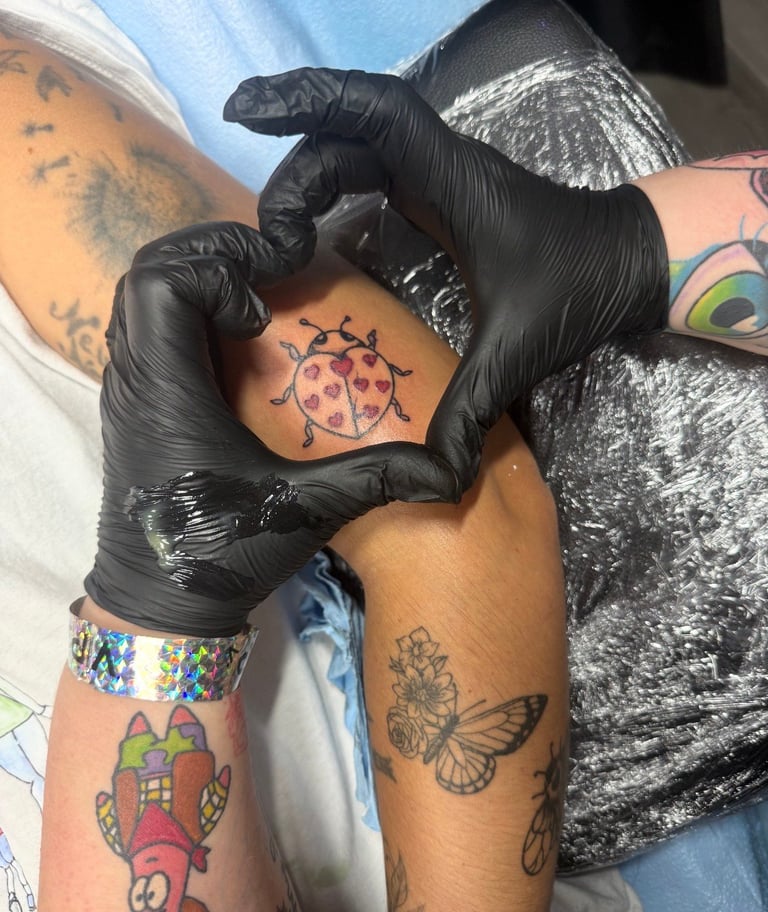 Tattoo artist in black gloves working on a client's arm, applying a red and black ladybug design tattoo