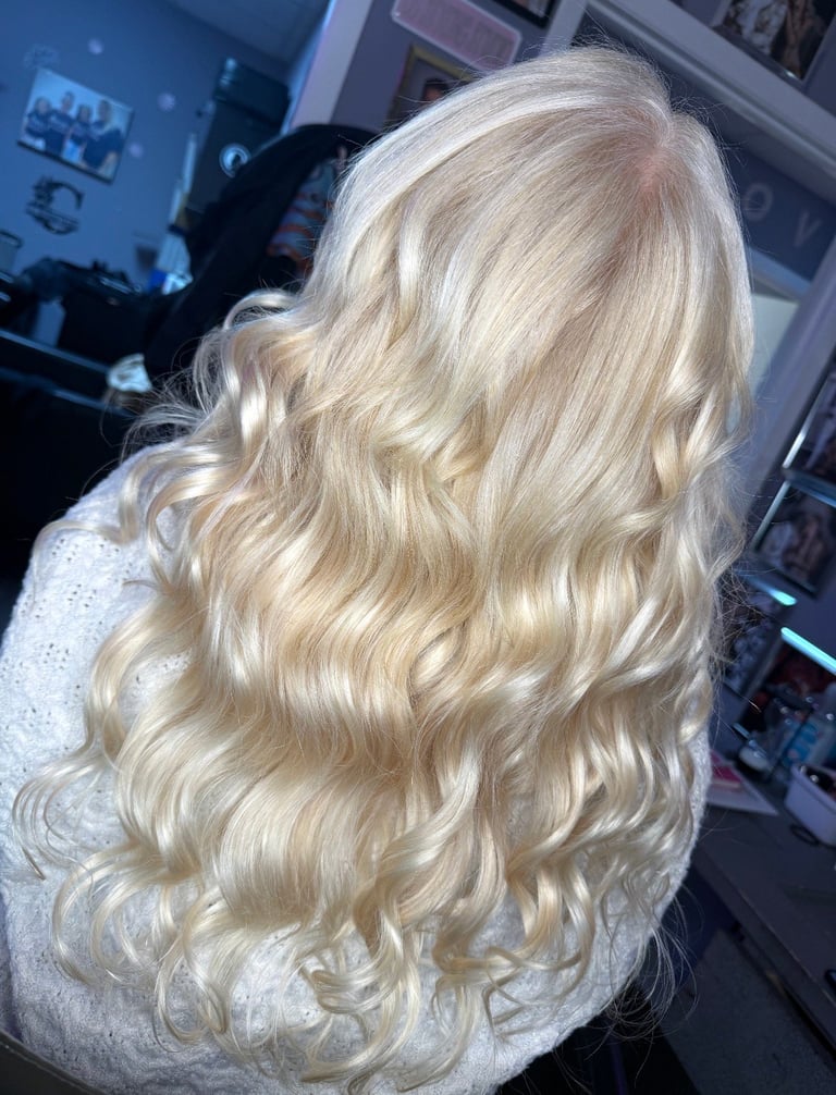 Back view of long blonde wavy hair with platinum blonde highlights in an indoor salon setting.