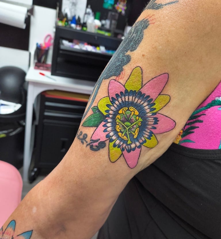 Close-up of a colorful flower tattoo on someone's arm with pink, yellow, and green petals and a detailed center