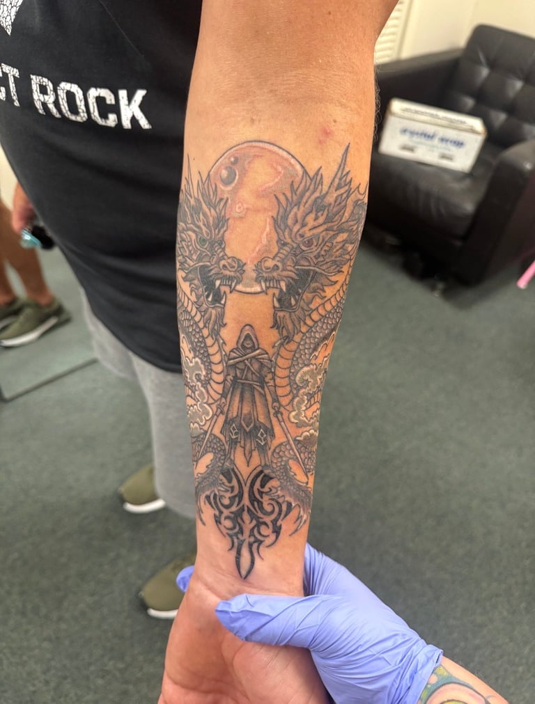 Person displaying a detailed black and gray tattoo on their forearm featuring a phoenix and ornamental design elements
