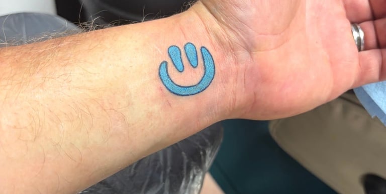 Blue power button smiley face tattoo on forearm of person's outstretched hand