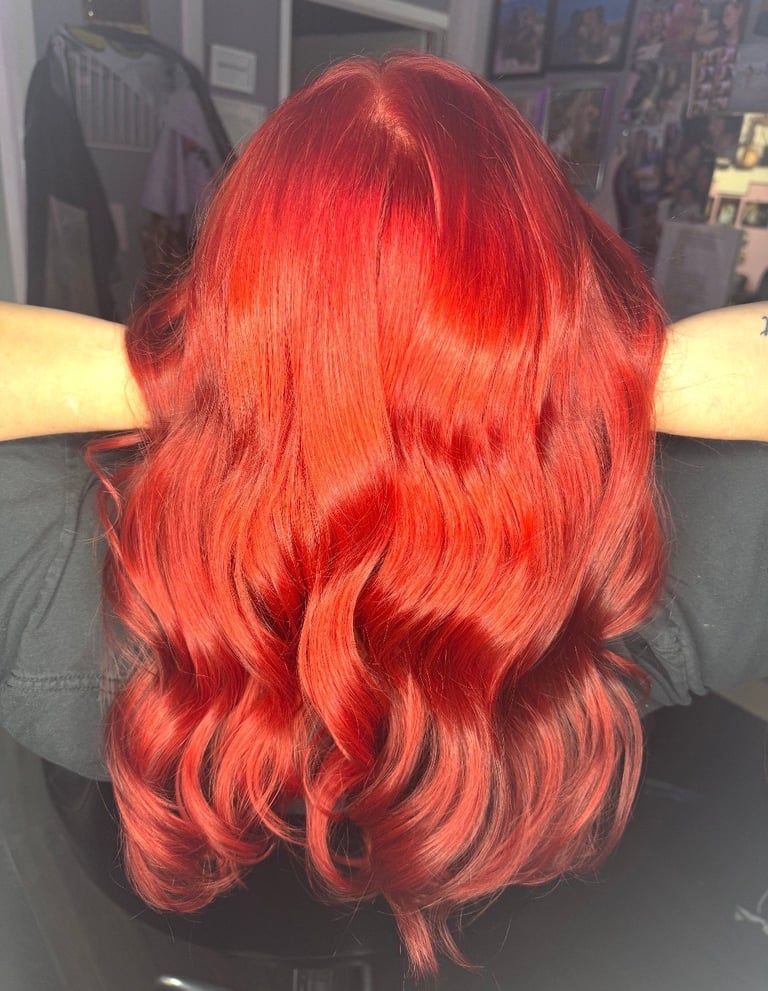 Full color red hair at CC Styling Studio in Bradenton, FL — back view of person with vibrant red wavy shoulder-length hair in a salon setting with warm lighting