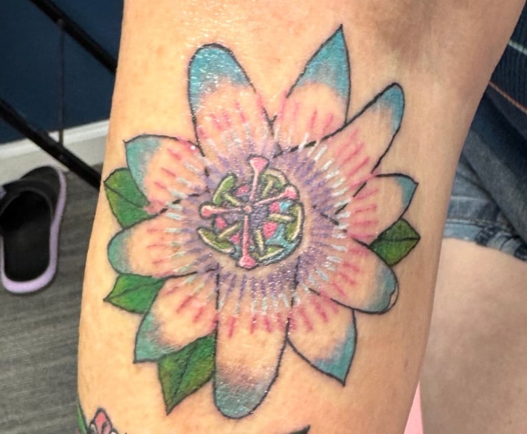Colorful passionfruit flower tattoo with pink, blue, and purple petals on skin