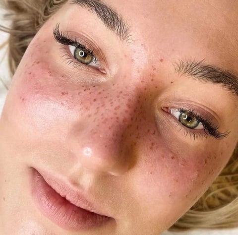 Close-up portrait of a woman with freckles, fair skin, and dramatic eye makeup looking directly at camera