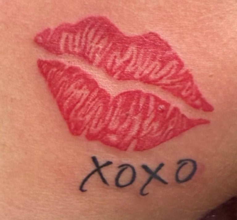 Red lipstick kiss mark tattoo with xoxo text written below on skin