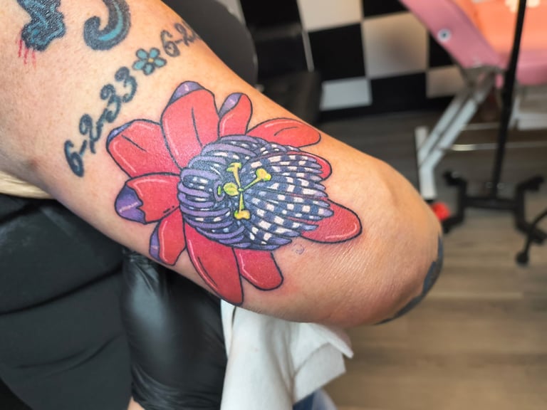 Colorful tattoo on arm featuring red flower petals with blue and yellow center, next to other text tattoos