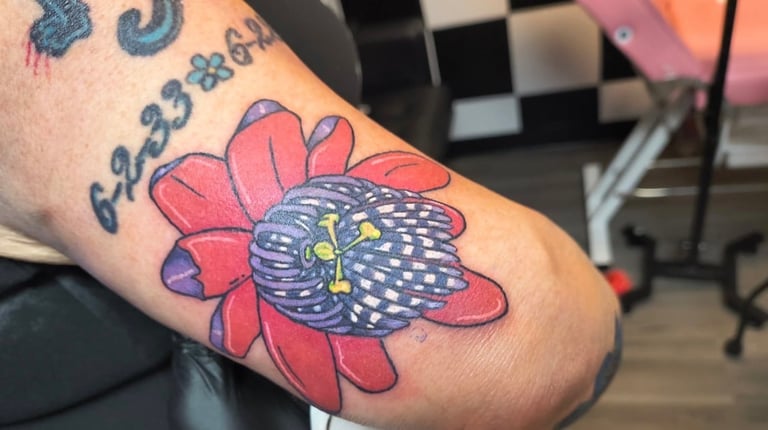 Colorful tattoo on arm featuring a blue patterned bee or insect on a pink flower with text above