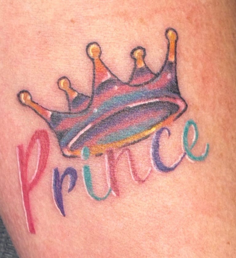 Colorful tattoo of a crown with rainbow gradient and the word Prince written below it in multicolored letters on skin