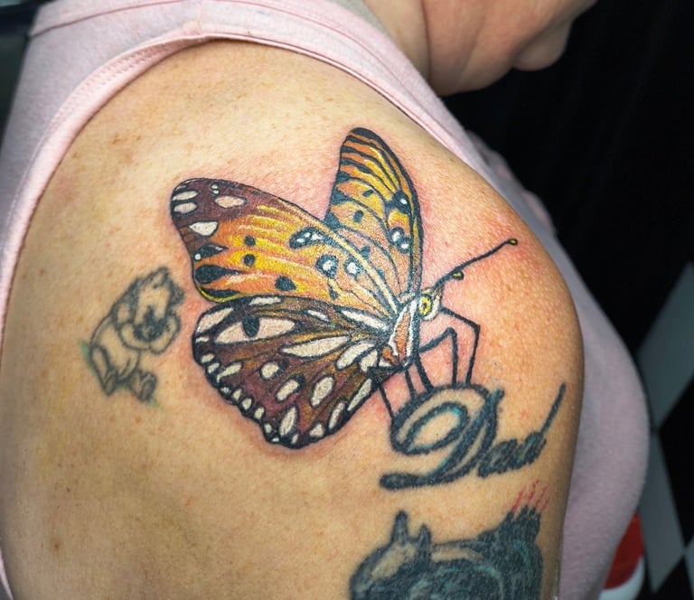 Colorful butterfly tattoo on person's arm with yellow and black wings, surrounded by smaller tattoo designs