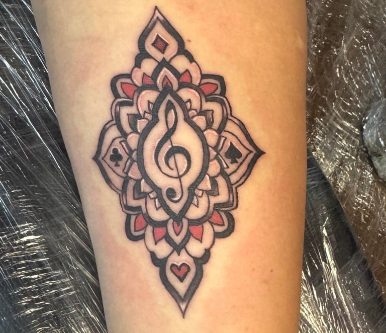 Tattoo of a treble clef inside a decorative mandala design with pink accents and heart symbol on skin