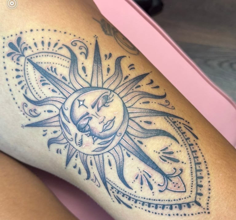Blue ink tattoo on arm featuring a crescent moon face surrounded by ornate sun rays and decorative celestial patterns