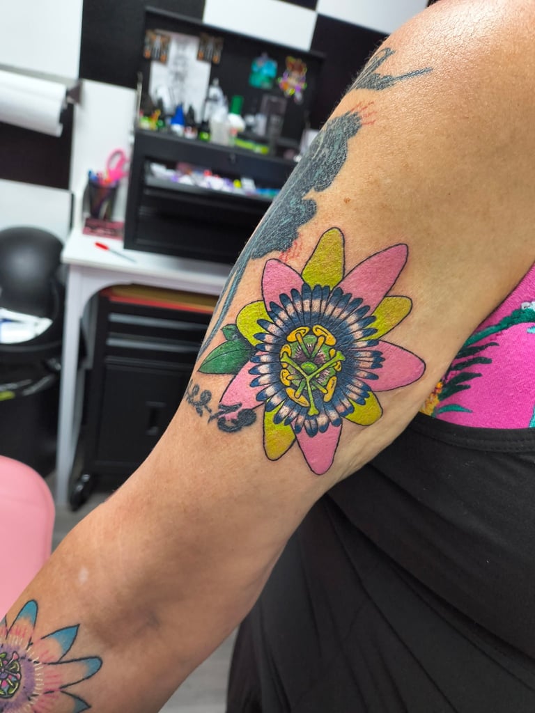 Close-up of colorful flower tattoo on person's arm with pink, yellow, and green petals in a tattoo studio setting