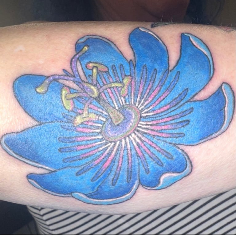 Blue stylized flower tattoo on arm with purple and pink stamens details