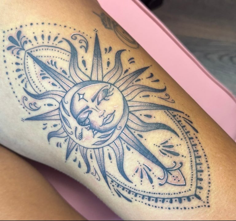 Blue ink tattoo on arm featuring a celestial design with a crescent moon face surrounded by radiating sun rays and ornate mandala-style decorative elements
