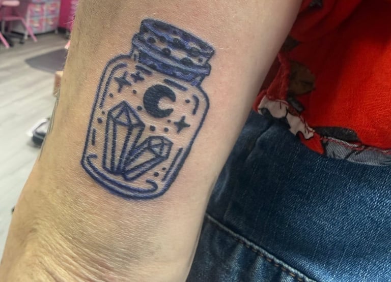 Blue line tattoo on forearm depicting a glass jar with moon and star design inside
