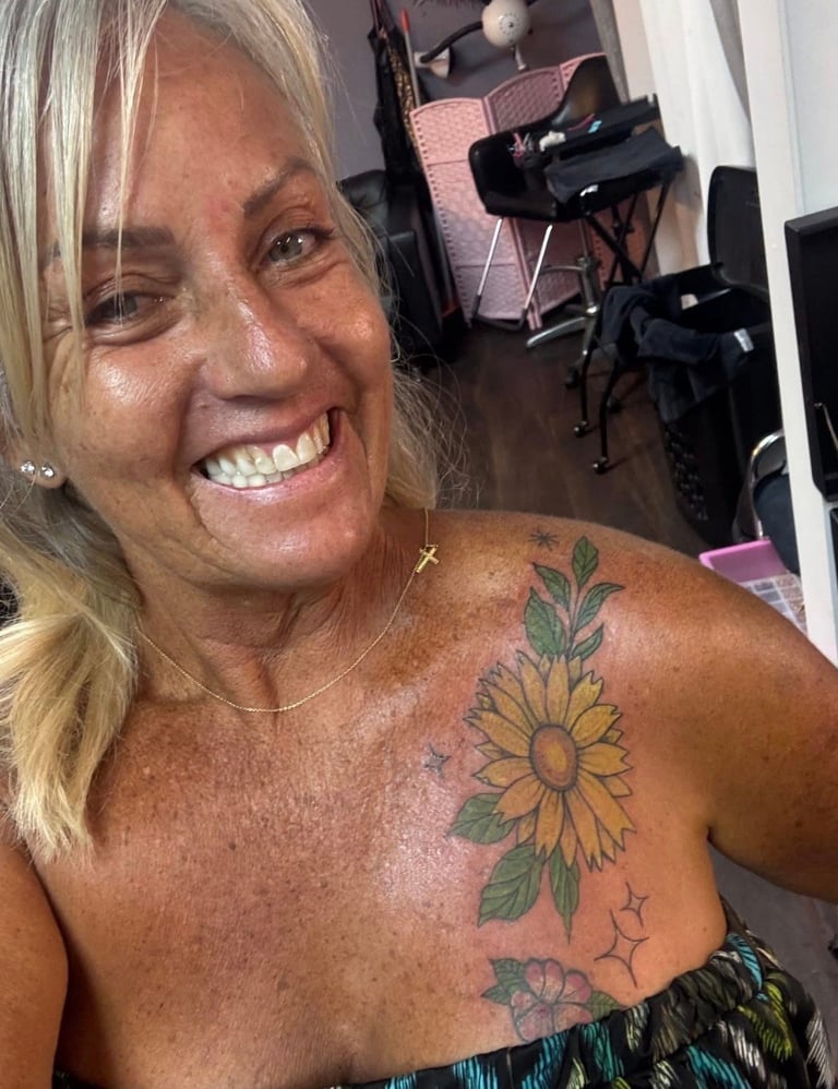 Woman smiling at camera displaying colorful tattoo sleeve with sunflower and botanical designs on her shoulder and arm