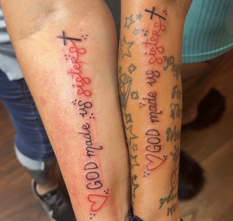 Close-up of two arms displaying matching tattoos with red cursive text, black crosses, and decorative elements