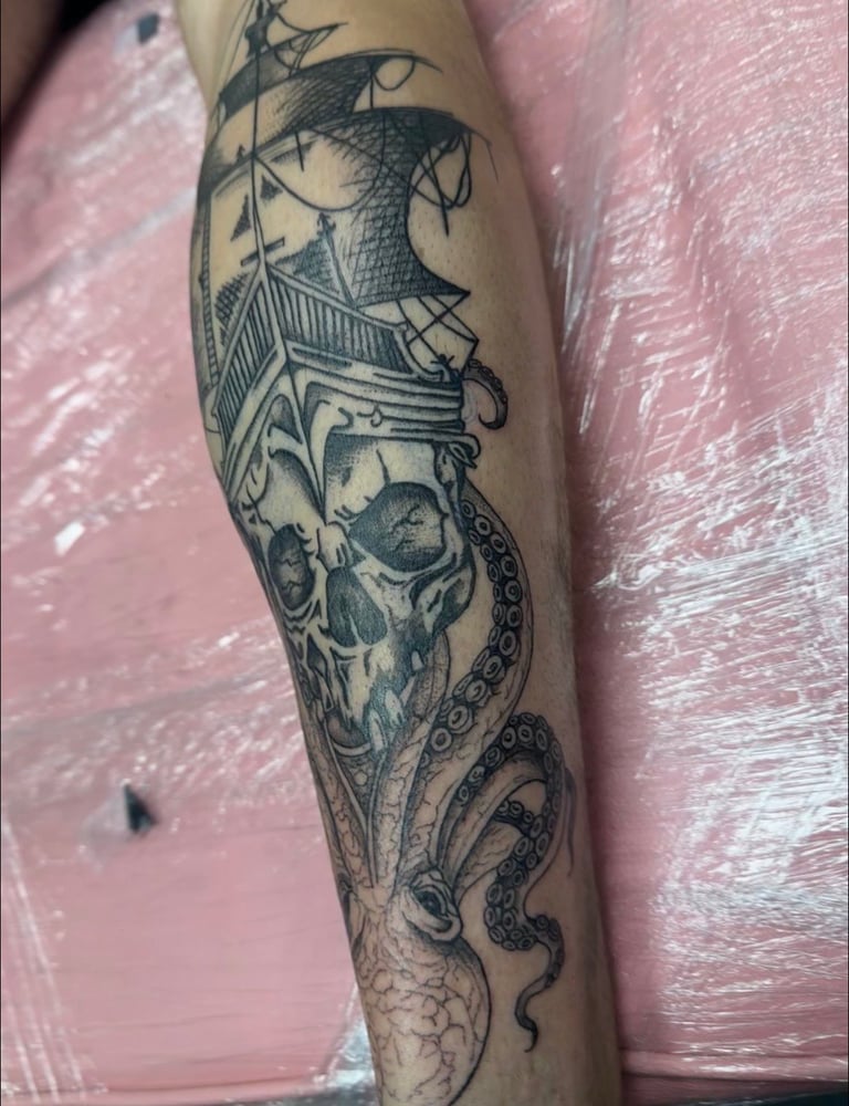 Tattoo on arm featuring a detailed design with a ship, skull, architectural elements, tentacles, and decorative patterns in black ink