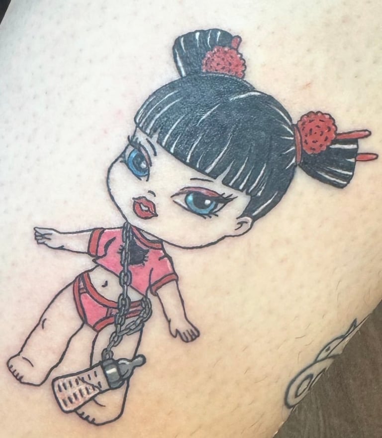 Tattoo of an anime-style girl character with dark hair buns, blue eyes, pink outfit, and holding a small weapon on skin