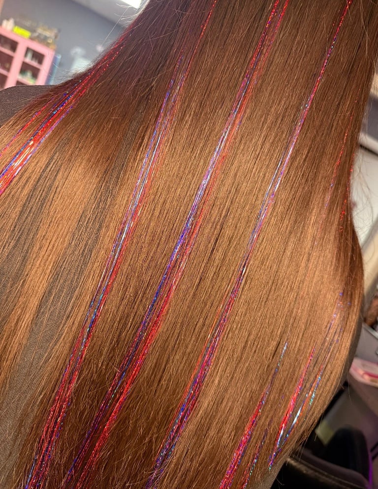 Close-up of long brown hair with colorful tinsel highlights in pink, purple, and blue woven through the strands