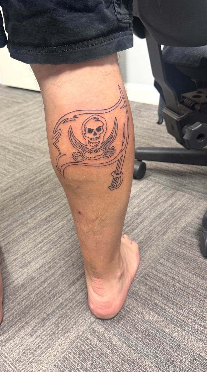 Person's calf with a pirate skull and crossed swords tattoo, wearing black shorts and white sneakers
