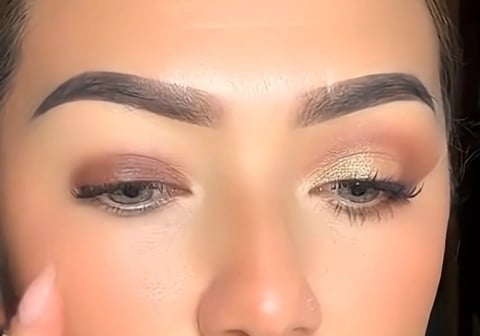 Close-up of womans face showing makeup with nude and gold eyeshadow, defined eyebrows, and natural complexion