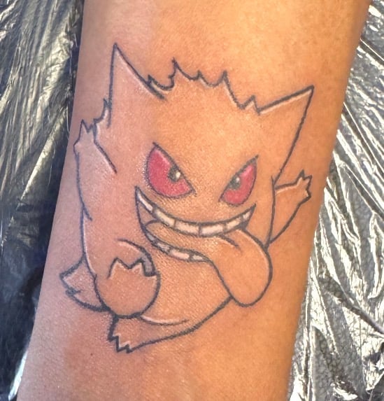 Tattoo of Haunter Pokemon character with red eyes and mischievous grin on person's arm