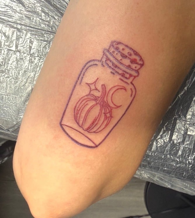 Purple outline tattoo on arm of a potion bottle with pumpkin, moon, and stars inside