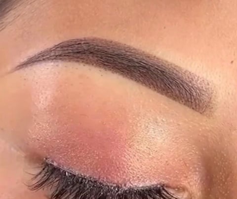 Close-up of a womans eye with pink eyeshadow, defined brown eyebrow, and black eyelashes on closed eyelid